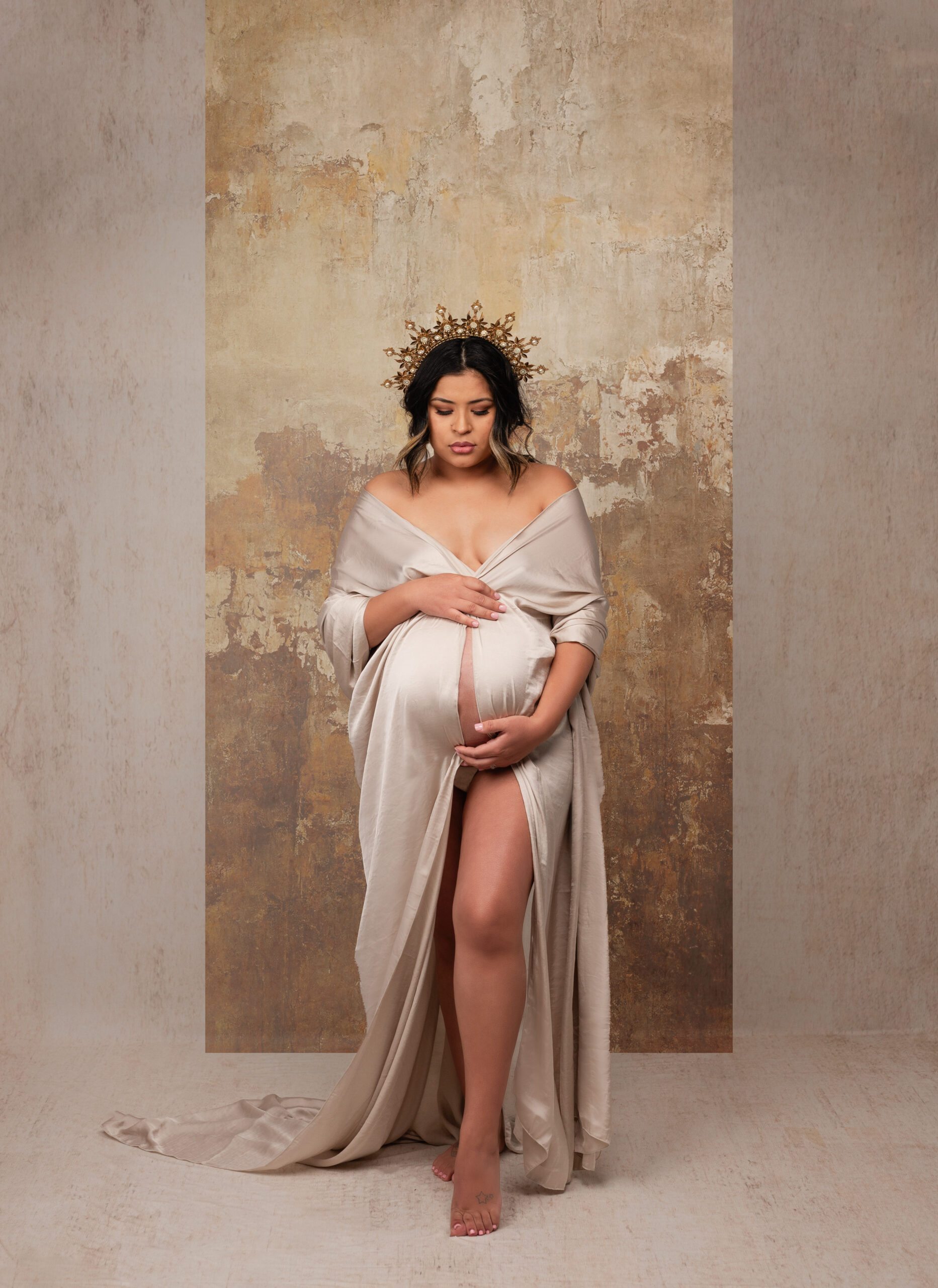 grand rapids maternity session pregnant woman holding her belly with gold crown on