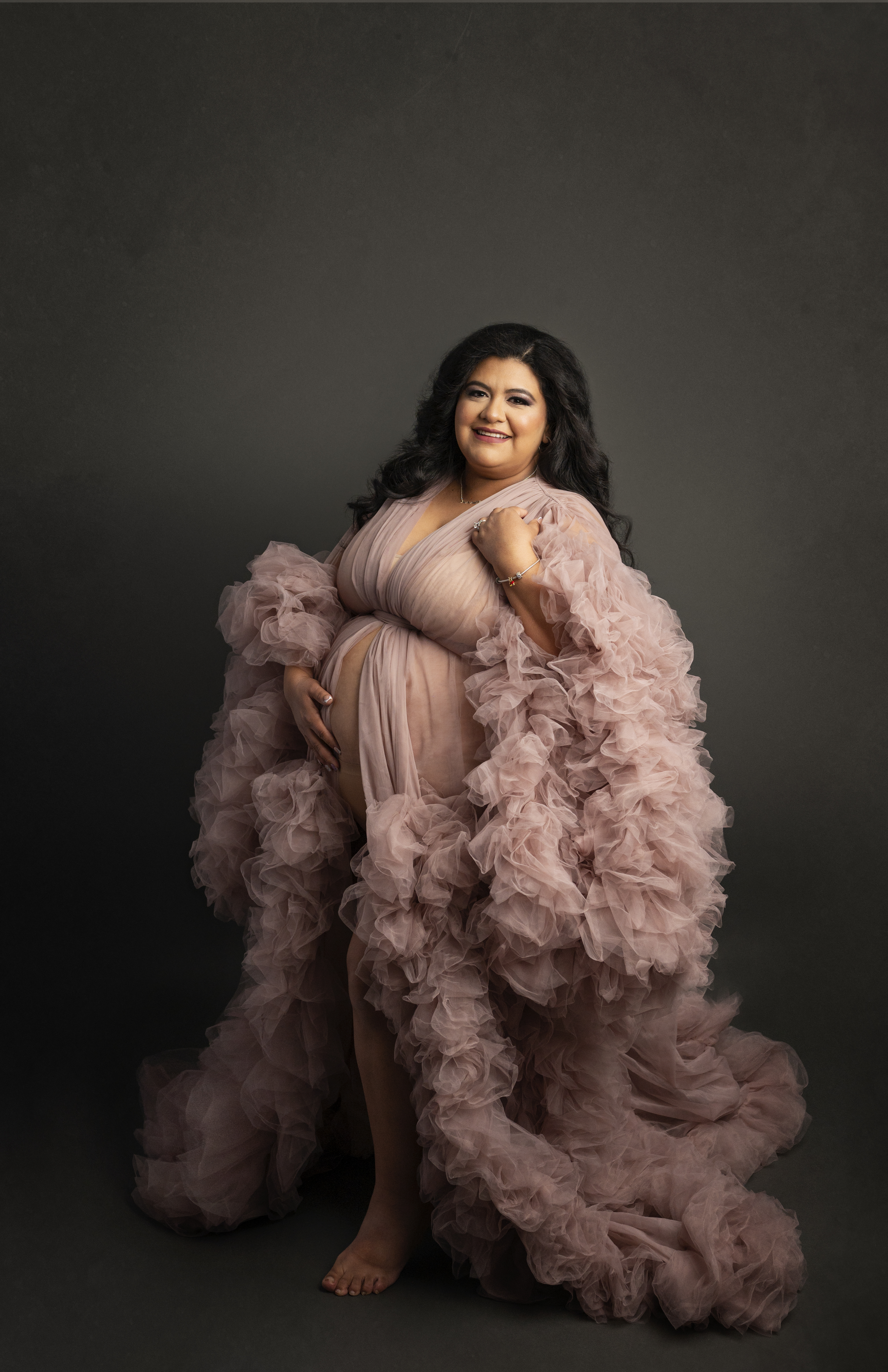Grand rapids maternity photo session woman in pink gown holding baby bump and smiling