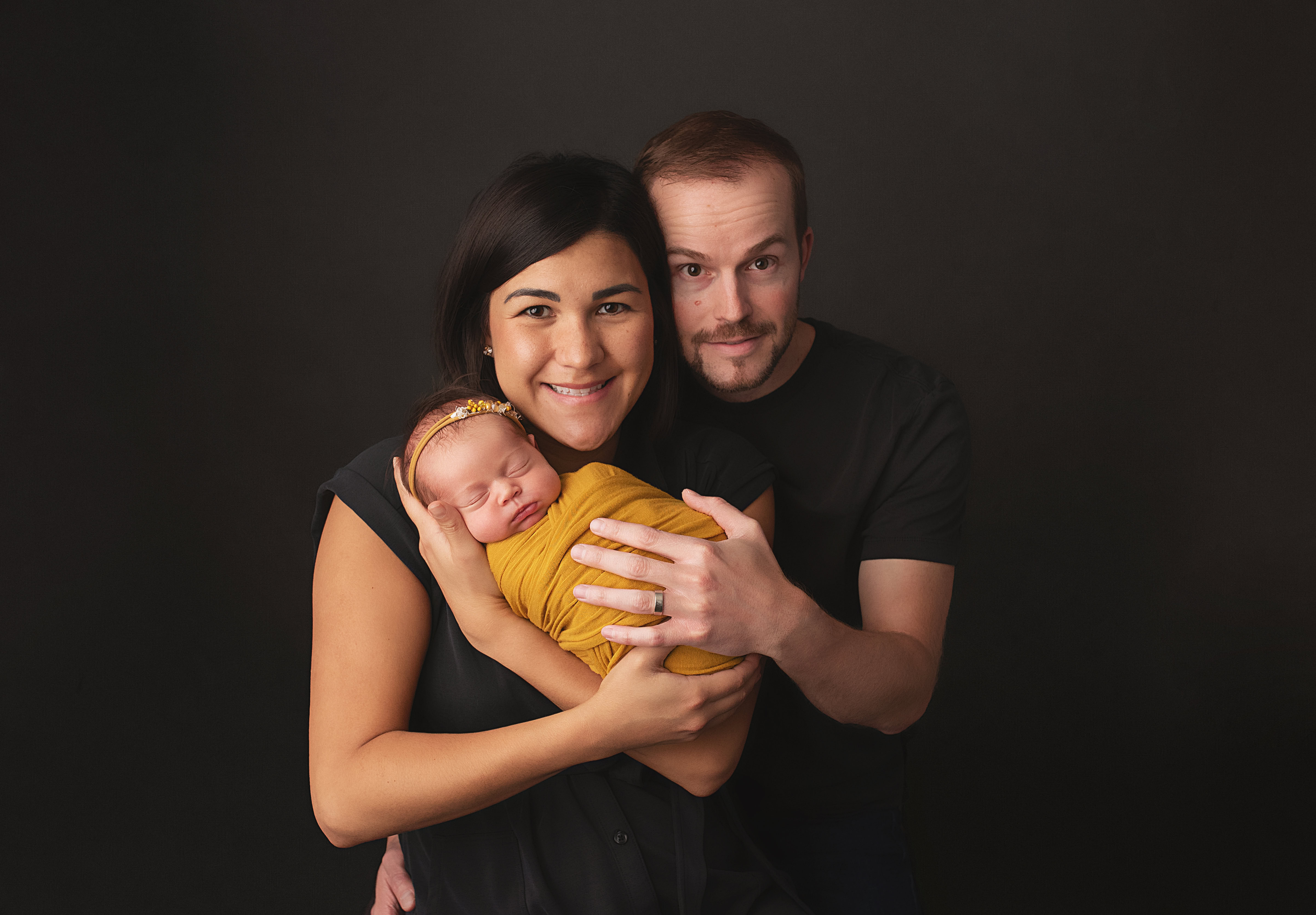 grand rapids newborn photo session mom and dad holding baby in golden swaddle