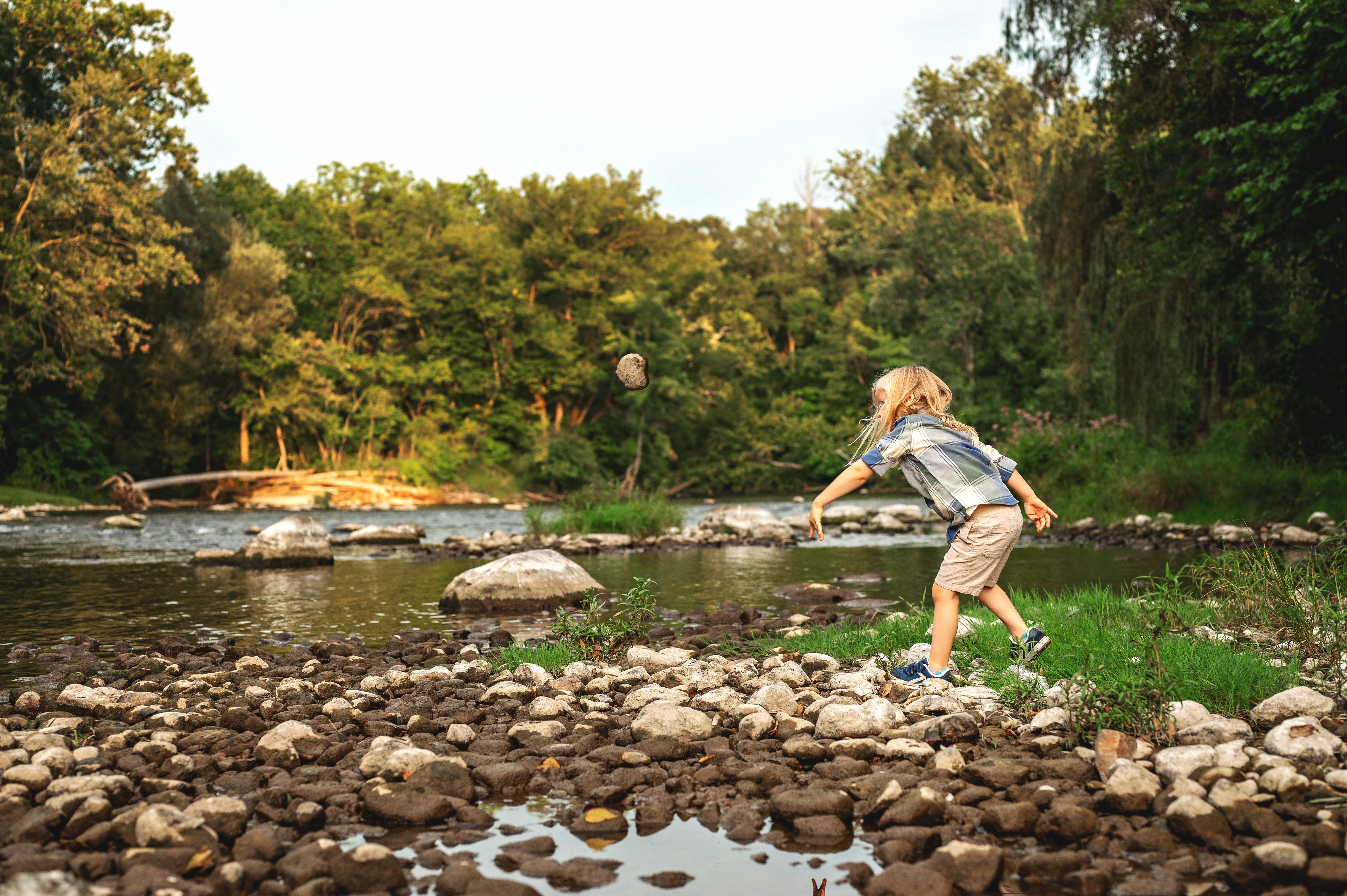 little boy throwing rocks in a river