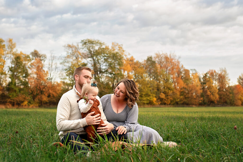 family of three sitting in a meadow and snuggling baby
