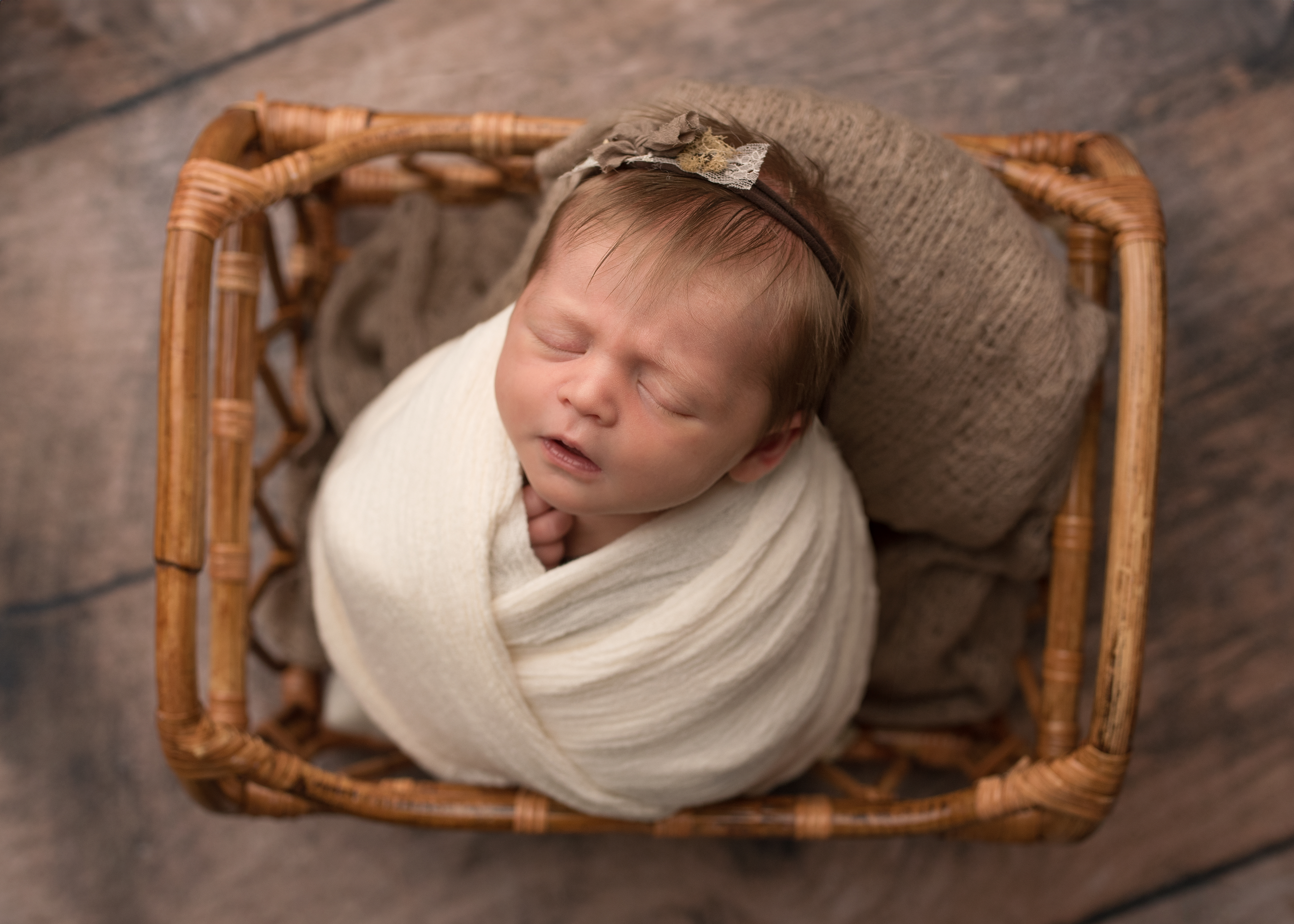 newborn photo session sleeping baby swaddled in cream wrap sleeping in brown basket