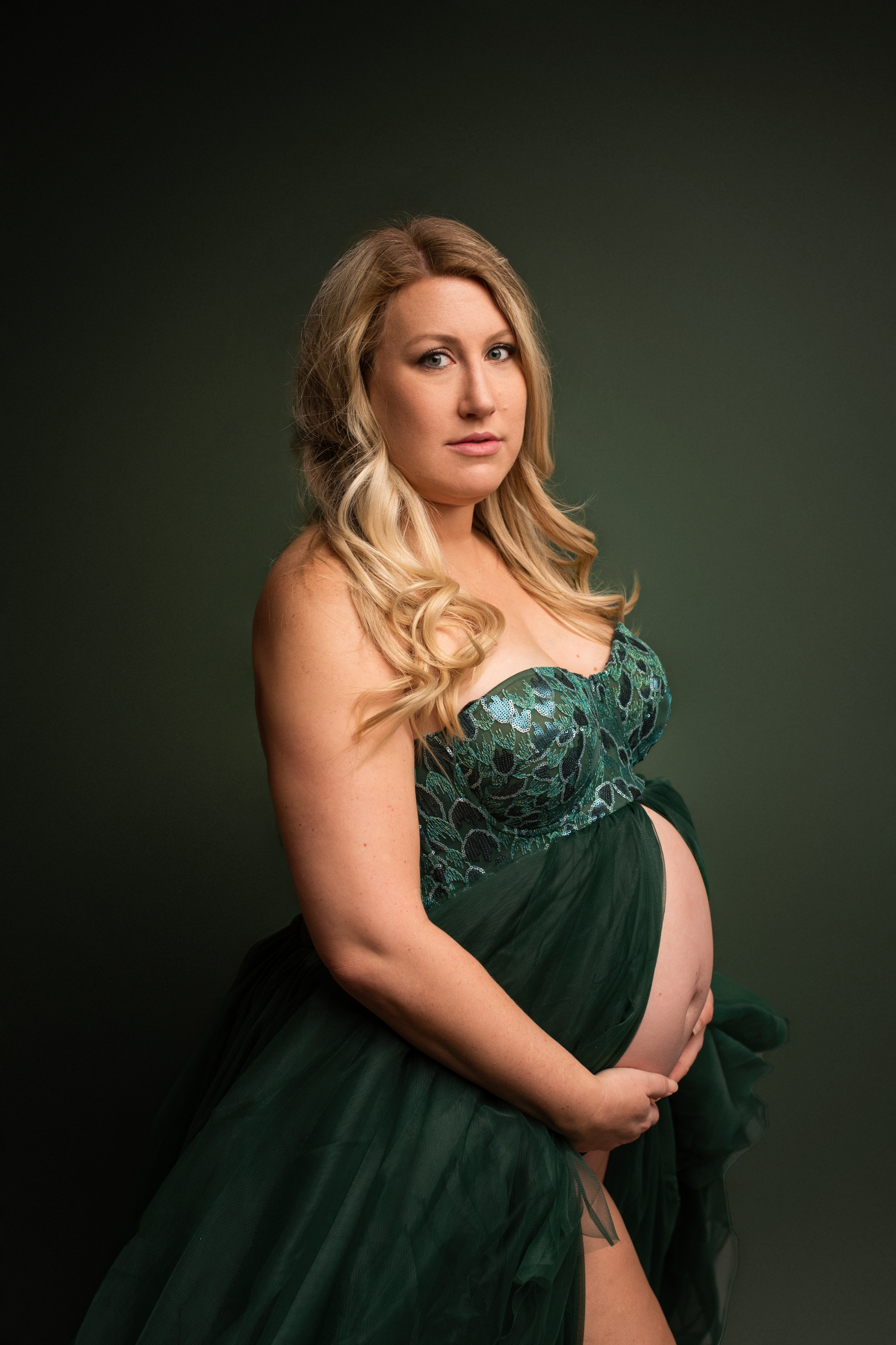 maternity photo session blonde woman wearing green dress looking at the camera