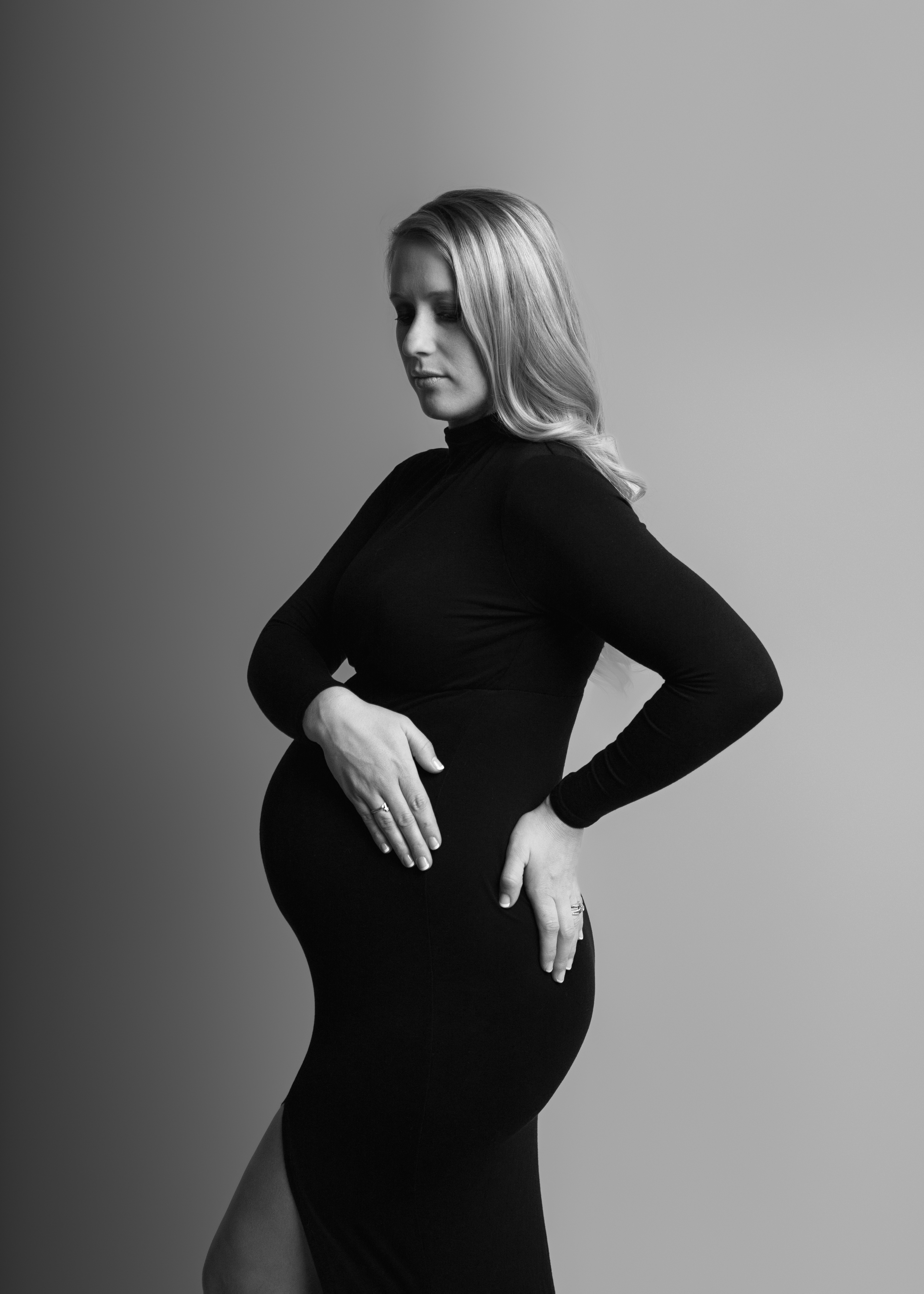 maternity photo session in grand rapids with a woman wearing a black dress and blonde hair looking down in black and white