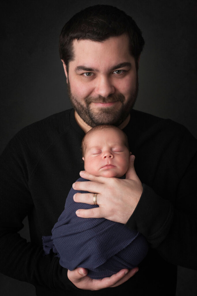 Newborn Photography, father holding baby against his chest, facing out toward camera